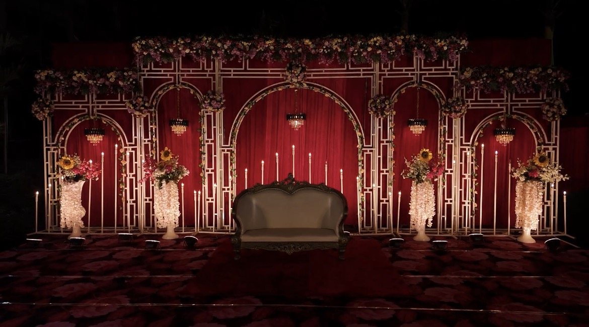 Abhinandan Palace wedding stage with white lattice arches, red drapes, chandeliers, candles and floral arrangements