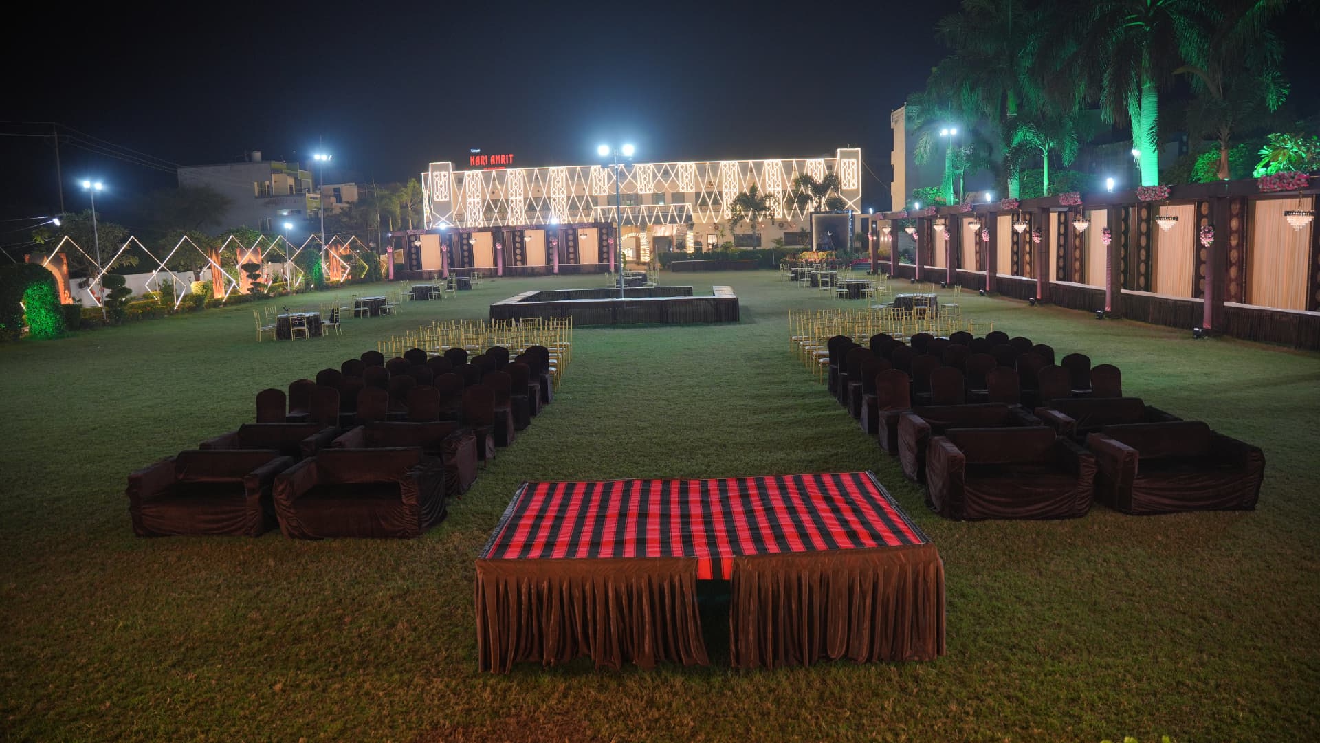 Wide view of the Hari Amrit lawn at night with sofa seating and the lit resort building