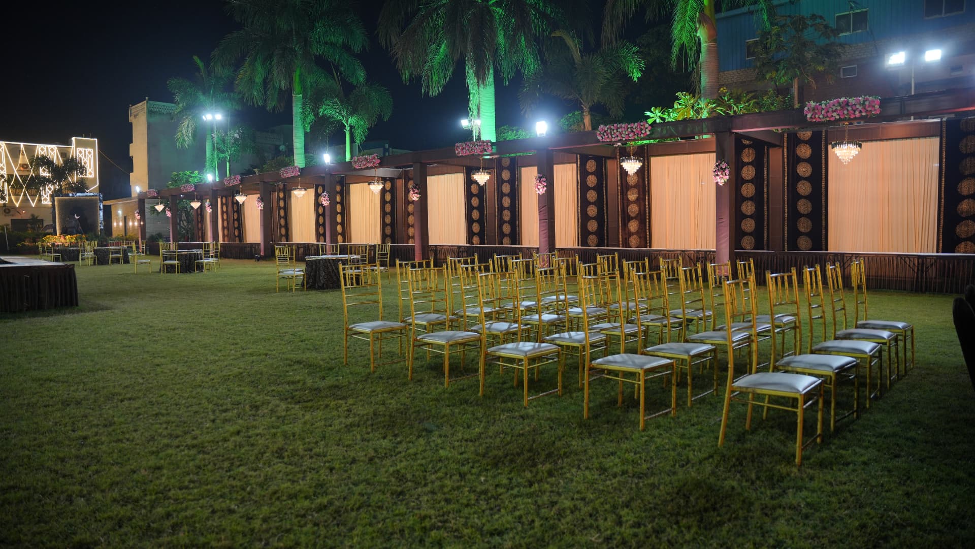 Rows of gold chairs on the Hari Amrit lawn at night, with lit pavilions along the edge