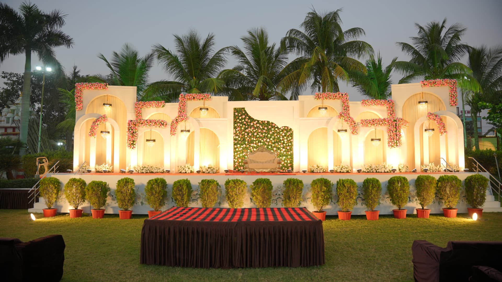 Hari Amrit wedding stage with white arches, pink florals and palm trees at dusk