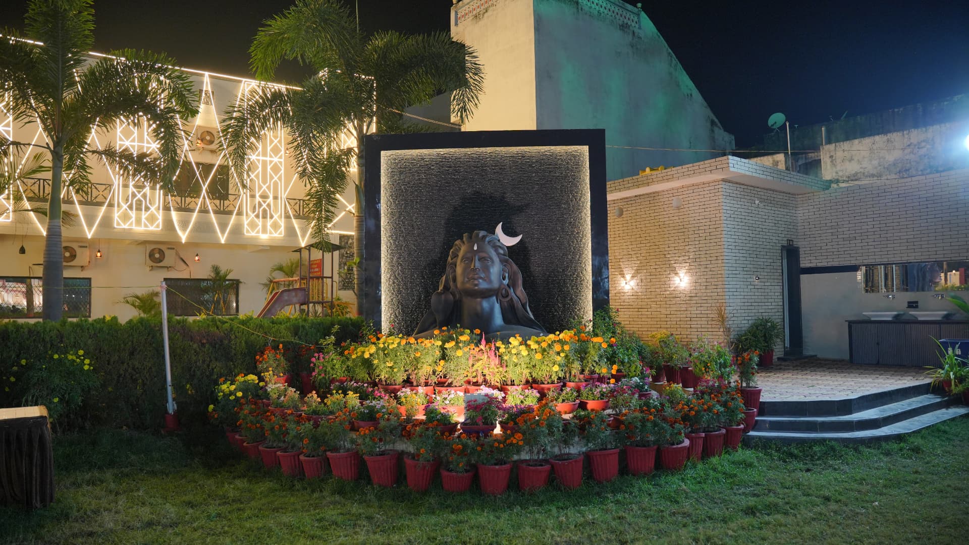 Illuminated Lord Shiva statue surrounded by marigold flower pots in the Hari Amrit garden